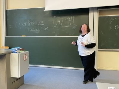 Donna Benjamin stands in front of a blackboard with OpenPracticeLibrary.com written on it - Photo by Angela "webchick" Byron