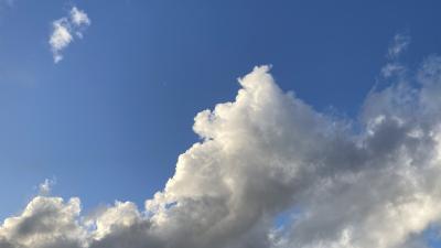 Clouds in a blue sky, with earth's tiny crescent moon.