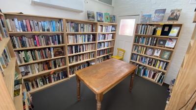 Bookshop interior. Walls lined with bookshelves, and a wooden table at the centre. 