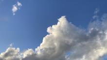 Clouds in a blue sky, with earth's tiny crescent moon.