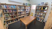 Bookshop interior. Walls lined with bookshelves, and a wooden table at the centre. 